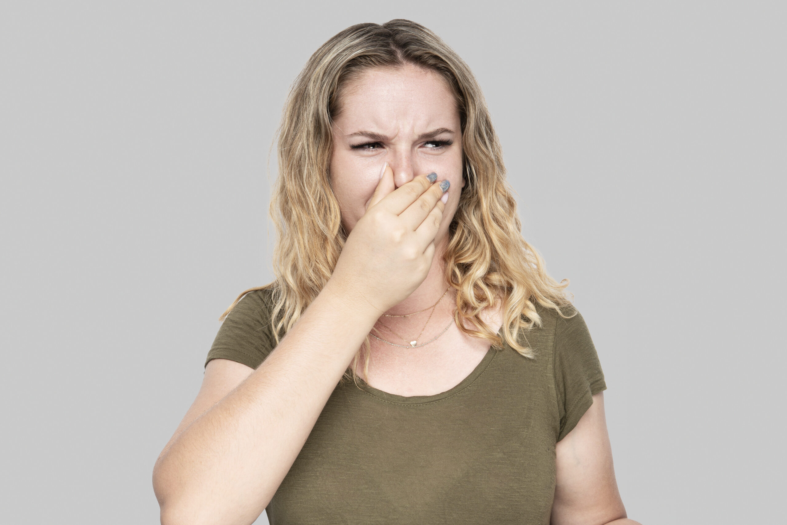 Girl covers nose with hand showing that something stinks isolated on gray background.